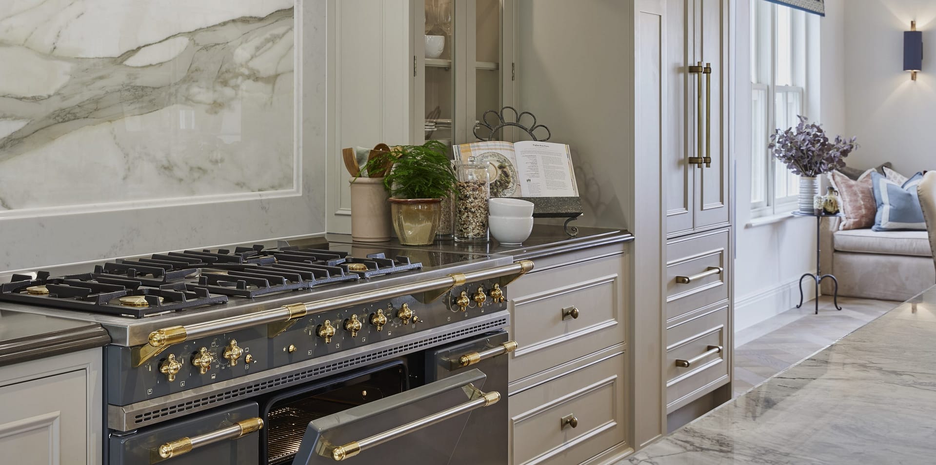 A Lacanche range oven integrated into a neutral kitchen and positioned in front of a marble splash back.